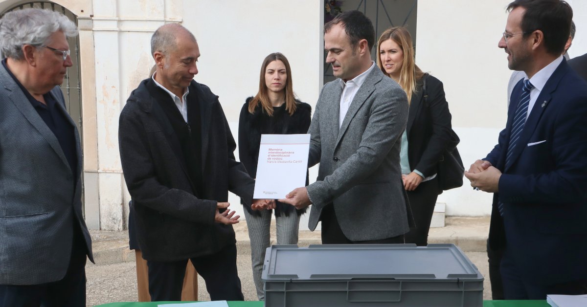 El director general de Memòria Democràtica, Alfons Aragoneses, entrega la memòria d'identificació de Narcís Mediavilla Cardó als seus néts, davant la capsa que conté les restes del soldat barceloní (Eloi Tost, ACN)