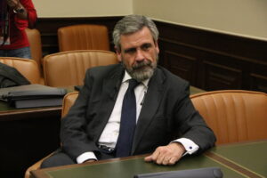 Hombre con barba y traje sentado en una sala con sillas de cuero