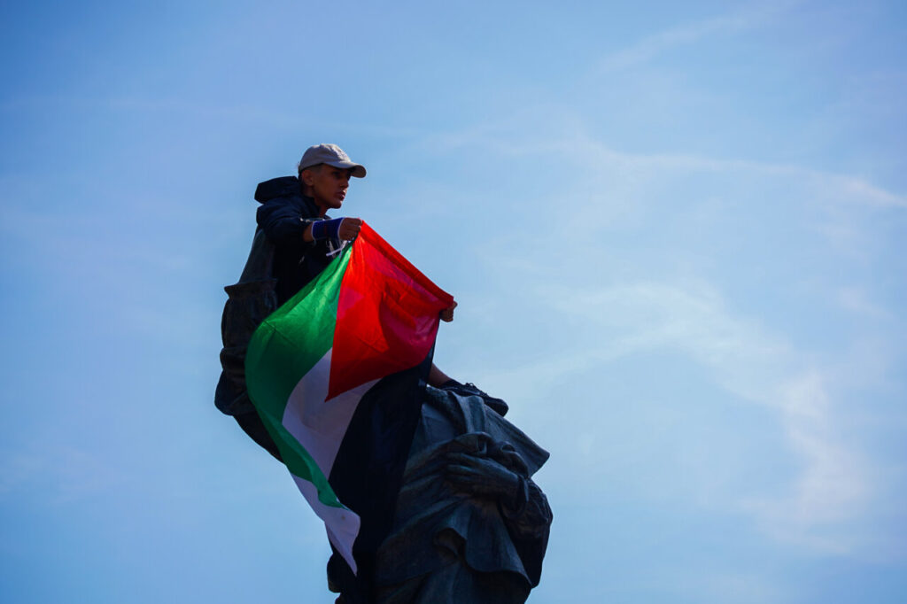 Un jove amb una bandera palestina enfilat en una estàtua