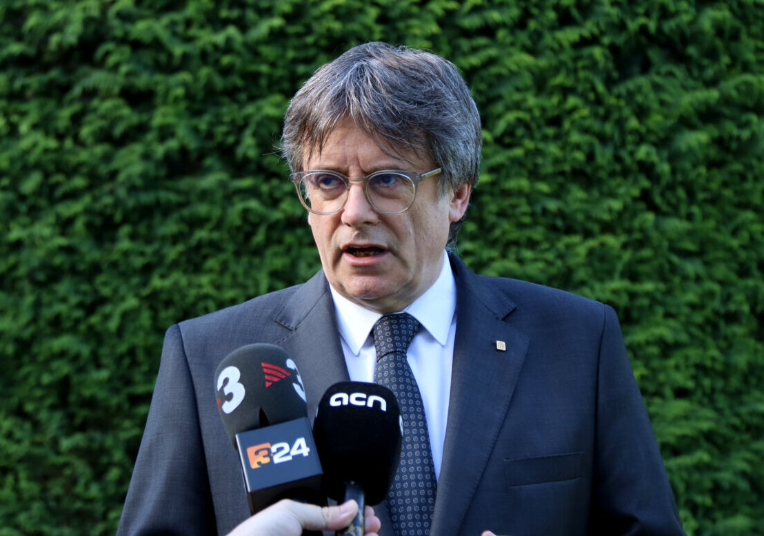 Carles Puigdemont parlant amb micròfons davant un fons verd
