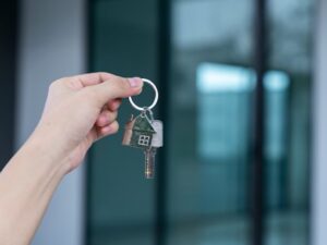 Una mà sosté claus amb un clauer de casa davant d'una finestra.