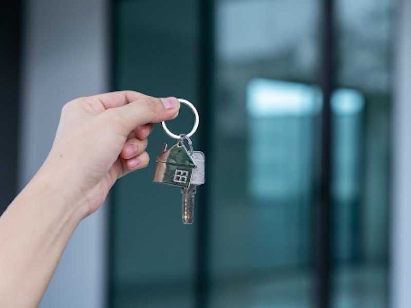 Una mà sosté claus amb un clauer de casa davant d'una finestra.