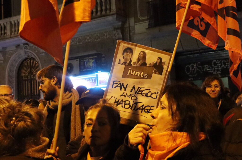 Cartell en una protesta contra Junts acusant-los de fer negoci amb l'habitatge.