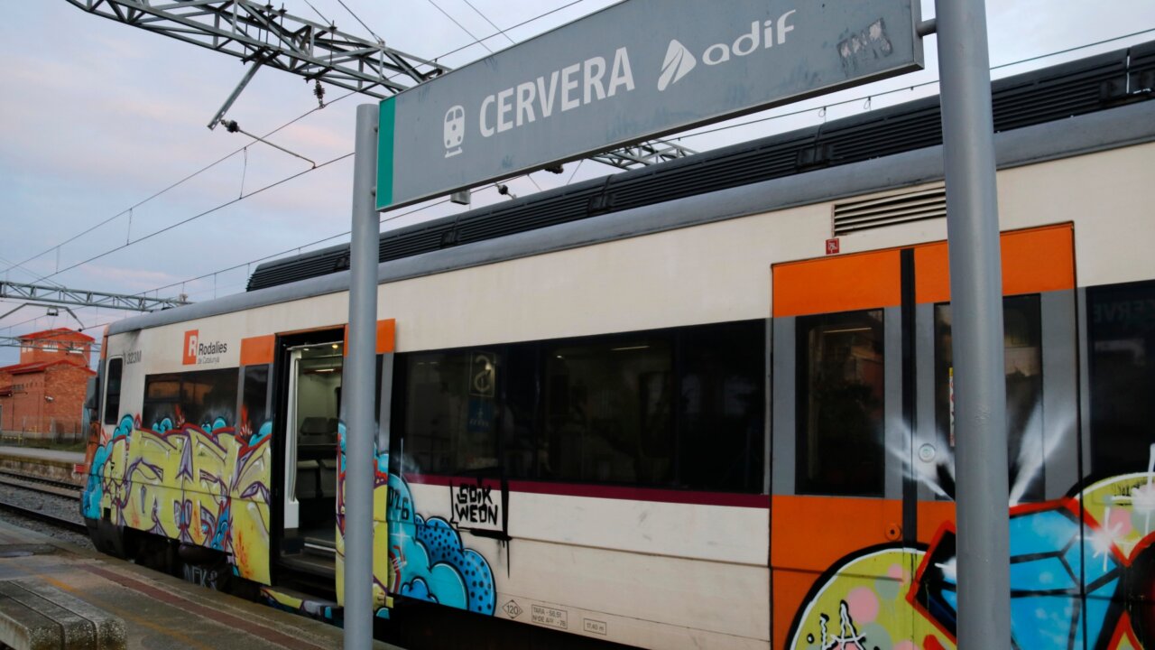 Un cartel de la parada de Cervera con un tren detrás (Anna Berga, ACN)