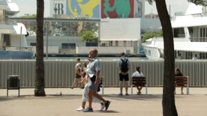 Dues persones passegen per la Barceloneta, amb publicitat de la Copa Amèrica de fons (Blanca Blay, ACN)